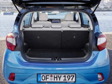 Achteraanzicht van een blauwe Hyundai i10 hatchback-auto met de kofferbak open, met de opbergruimte en neergeklapte achterbank.