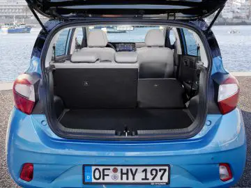 Blauwe Hyundai i10 hatchback met open kofferbak en ruime laadruimte aan het water.