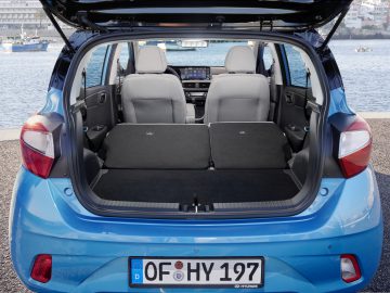 Weergave van een open kofferbak van een blauwe Hyundai i10 hatchback met de achterbank neergeklapt, waardoor de laadruimte zichtbaar is, met een haven op de achtergrond.
