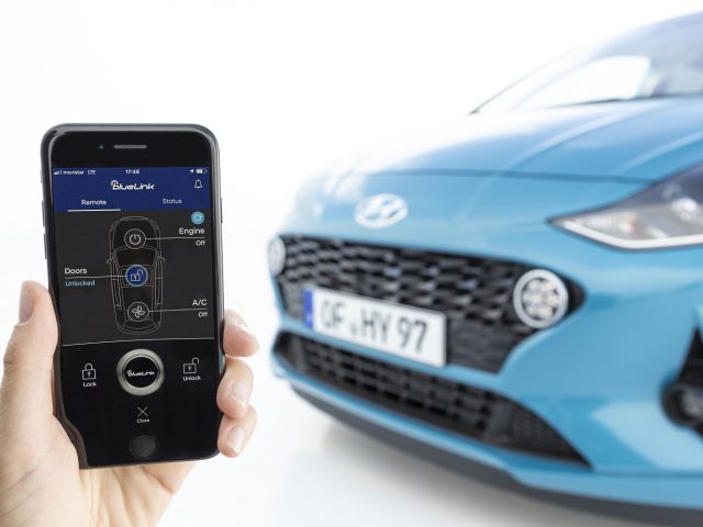 Hand met een smartphone met een autobedieningsapp voor een blauwe Hyundai i10.