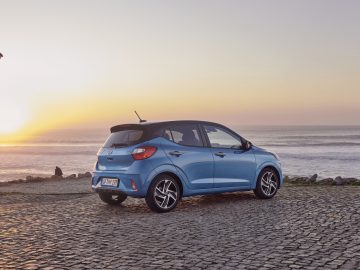 Een blauwe Hyundai i10 hatchback geparkeerd op een kustweg bij zonsondergang.