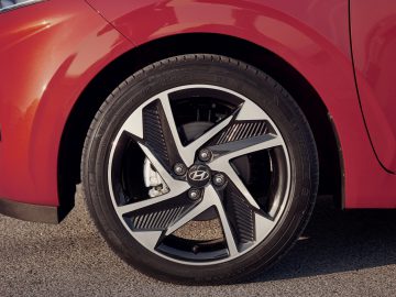 Het voorwiel van de rode Hyundai i10 met een gedetailleerd zicht op de lichtmetalen velg en band.