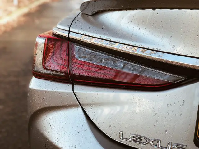 Close-up van het achterlicht en de kofferbak van een natte Lexus ES 300h met waterdruppels.