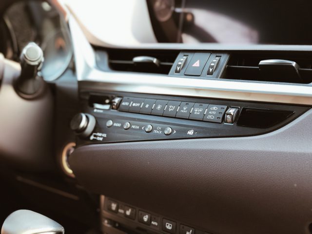 Binnenaanzicht van een Lexus ES 300h, gericht op de middenconsole met airconditioningbediening en multimediaknoppen.