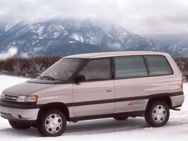 Een zilveren Mazda 4wd minivan geparkeerd op sneeuw met bergen op de achtergrond.