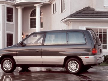 Een bruine Mazda-minibus geparkeerd voor een huis in een buitenwijk op een natte oprit.