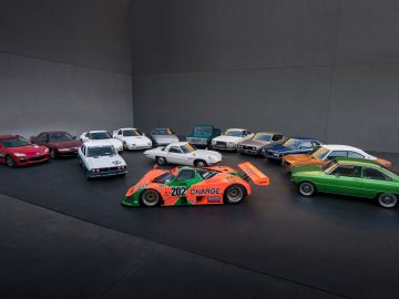 Een gevarieerde collectie klassieke en moderne sportwagens, waaronder Mazda-modellen, weergegeven in een halve cirkel op een minimalistische achtergrond.