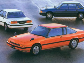 Drie vintage Mazda-auto's geparkeerd op een nat oppervlak, met verschillende carrosserievarianten uit hetzelfde autotijdperk.