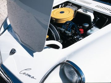 Witte vintage Mazda met open motorkap waardoor de motorruimte zichtbaar is.
