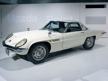 Vintage Mazda-sportwagen tentoongesteld in een tentoonstellingsomgeving met de tekst 'sportgeest' op de muur erachter.