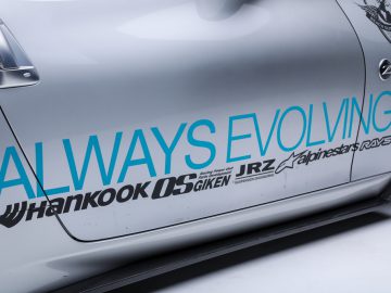 Zijaanzicht van een zilveren auto geïnspireerd op "The Fast and the Furious", met de uitdrukking "altijd in ontwikkeling" en verschillende sponsorlogo's.