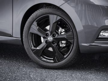 Close-up van een autoband met een zwarte lichtmetalen velg op een Nissan N-Tec-voertuig, met het Nissan-logo.