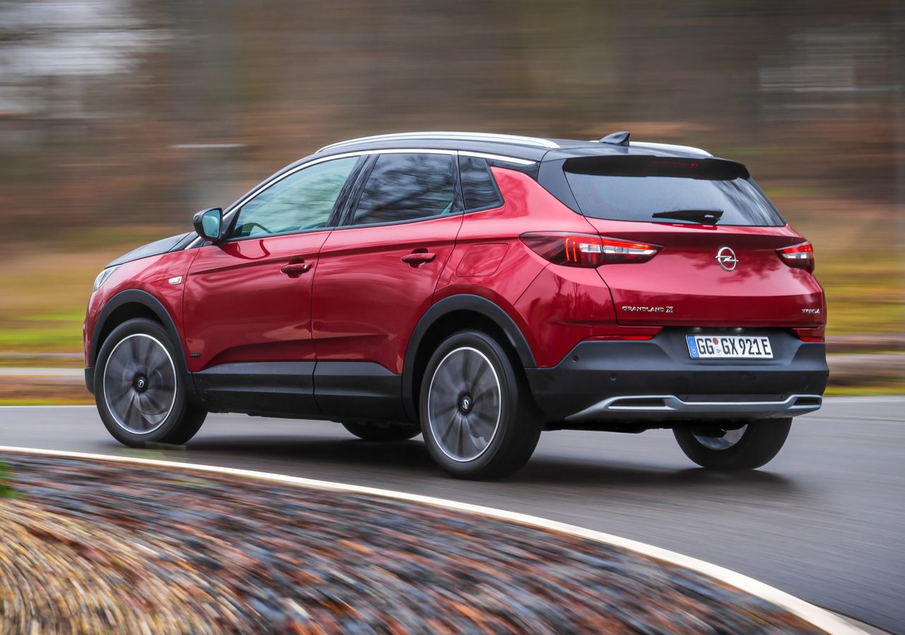 Een rode Opel Grandland X in beweging op een natte weg, die dynamisch rijgedrag laat zien.