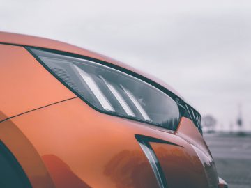 Close-up van het oranje voorspatbord en de led-koplampen van een Peugeot 2008 met een onscherpe achtergrond.