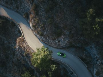 Luchtfoto van een bochtige weg met een enkele Porsche 718 GTS die door een bosrijke omgeving rijdt.