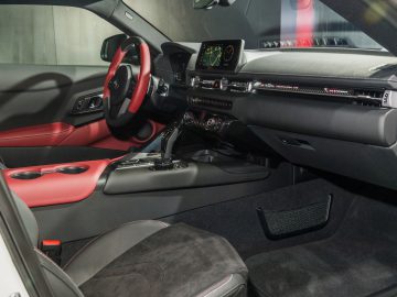 Binnenaanzicht van een Toyota GR Supra met rode en zwarte lederen bekleding, met een digitaal dashboard en touchscreen op de middenconsole.