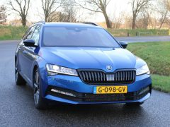 Blauwe Skoda Superb stationwagen geparkeerd op een weg met een met gras begroeide achtergrond overdag.