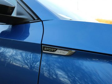Close-up van het zijpaneel van een blauwe Skoda Superb met een 'sport line'-badge.