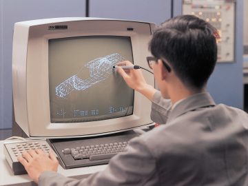 Een man die een stylus gebruikt om te communiceren met een Mazda-draadmodel van een auto op een vroeg computerwerkstation.