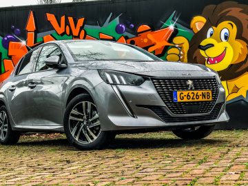 Een zilveren Peugeot 208-auto geparkeerd voor een levendige graffitimuur met kleurrijke ontwerpen en een leeuwillustratie.