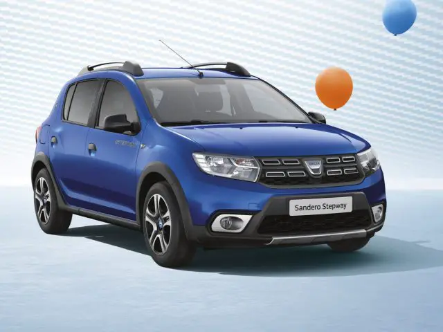Een blauwe Dacia Sandero Stepway geparkeerd met een achtergrond met patroon en zwevende ballonnen.