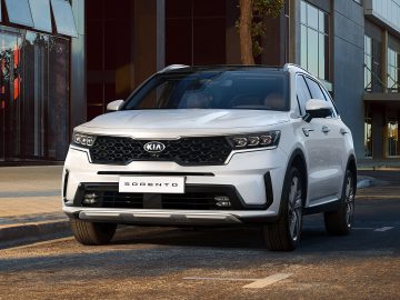 Een Kia Sorento geparkeerd voor een modern gebouw met glazen gevels overdag.