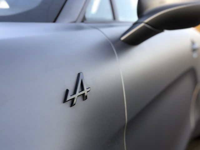 Een close-up van een metalen Alpine A110 S auto-embleem met een onscherpe achtergrond.