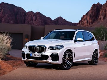 Een witte BMW X5 SUV geparkeerd op een woestijnweg met rotsachtig terrein op de achtergrond.