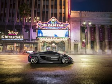 Een zwarte Czinger 21C-sportwagen geparkeerd voor het verlichte El Capitan Theater 's nachts.