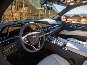 Binnenaanzicht van een moderne Cadillac Escalade met focus op het stuur en het dashboard, in zonlicht met een woestijnlandschap zichtbaar buiten de ramen.