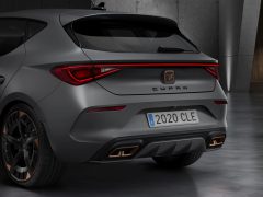 Achteraanzicht van een grijze Cupra Leon-hatchback uit 2020 met dubbele uitlaten in een showroom.