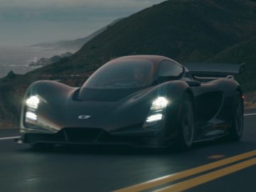 Een Czinger 21C die in de schemering langs een kustweg rijdt.