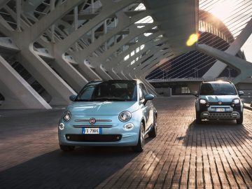 Twee Fiat 500 hybride auto's geparkeerd op een moderne brug bij zonsondergang.