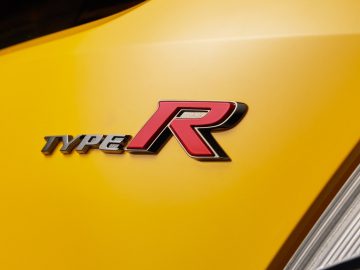 Close-up van het voorpaneel van een gele Honda Civic met een 'Type R'-badge.