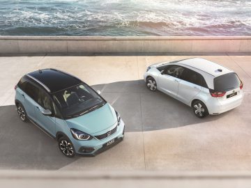 Twee moderne Honda Jazz-auto's naast elkaar geparkeerd op een betonnen ondergrond vlakbij de oceaan.