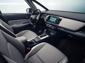 Modern Honda Jazz-interieur met een touchscreen-infotainmentsysteem, automatische versnellingspook en een tweekleurig dashboardontwerp.