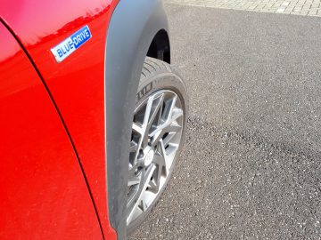 Rode Kona Hybrid met een "bluedrive" -badge geparkeerd op een verhard oppervlak, met de nadruk op het voorwiel.