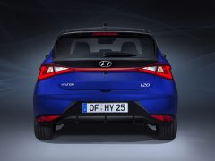 Achteraanzicht van een blauwe Hyundai i20 geparkeerd met de lichten aan tegen een donkere achtergrond.