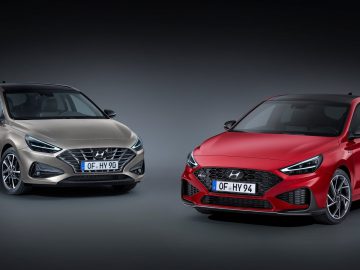 Twee moderne Hyundai i30 hatchback-auto's op een donkere achtergrond, een zilveren en een rode, die hun ontwerp en styling laten zien.
