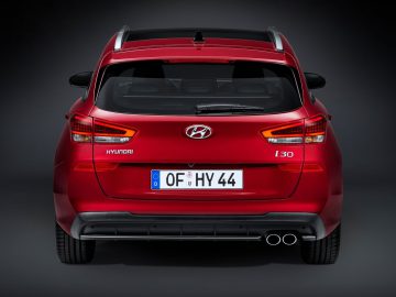 Achteraanzicht van een rode Hyundai i30 tegen een grijze achtergrond.