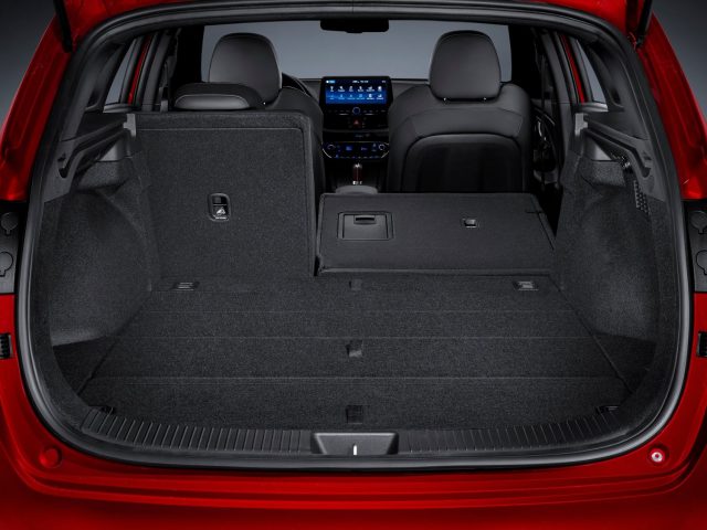 Ruime en lege kofferbak van een moderne rode Hyundai i30 met neergeklapte achterbank, waardoor de bagageruimte en het interieurontwerp goed tot hun recht komen.