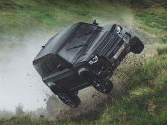 Land Rover Defender springt dynamisch in de lucht over ruw terrein met rondvliegend vuil.