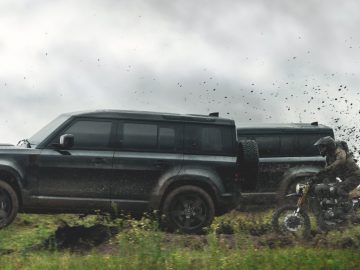 Land Rover Defender en motorrijder door ruw terrein met opspattende modder.