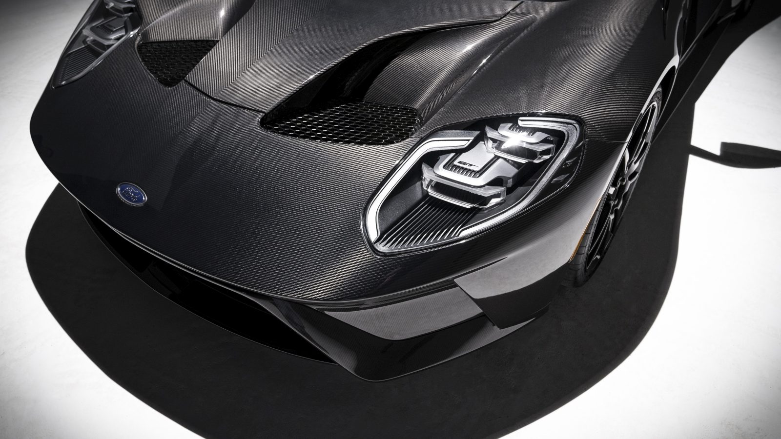 Close-up van een zwarte koolstofvezel Ford GT sportwagenkap en badge.