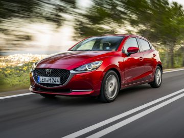 Rode Mazda 2 hatchback-auto in beweging op een weg.
