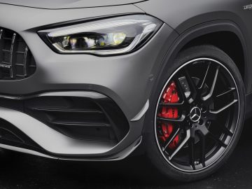 Close-up van het voorwiel en de koplamp van een moderne Mercedes-AMG GLA 45 4MATIC+, waarbij het ontwerp van de lichtmetalen velgen en de rode remklauwen benadrukt worden.