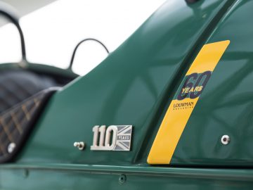 Close-up van het zijpaneel van een vintage Morgan groene auto, met het jubileumbadge "60 jaar" en het embleem "110 jaar".