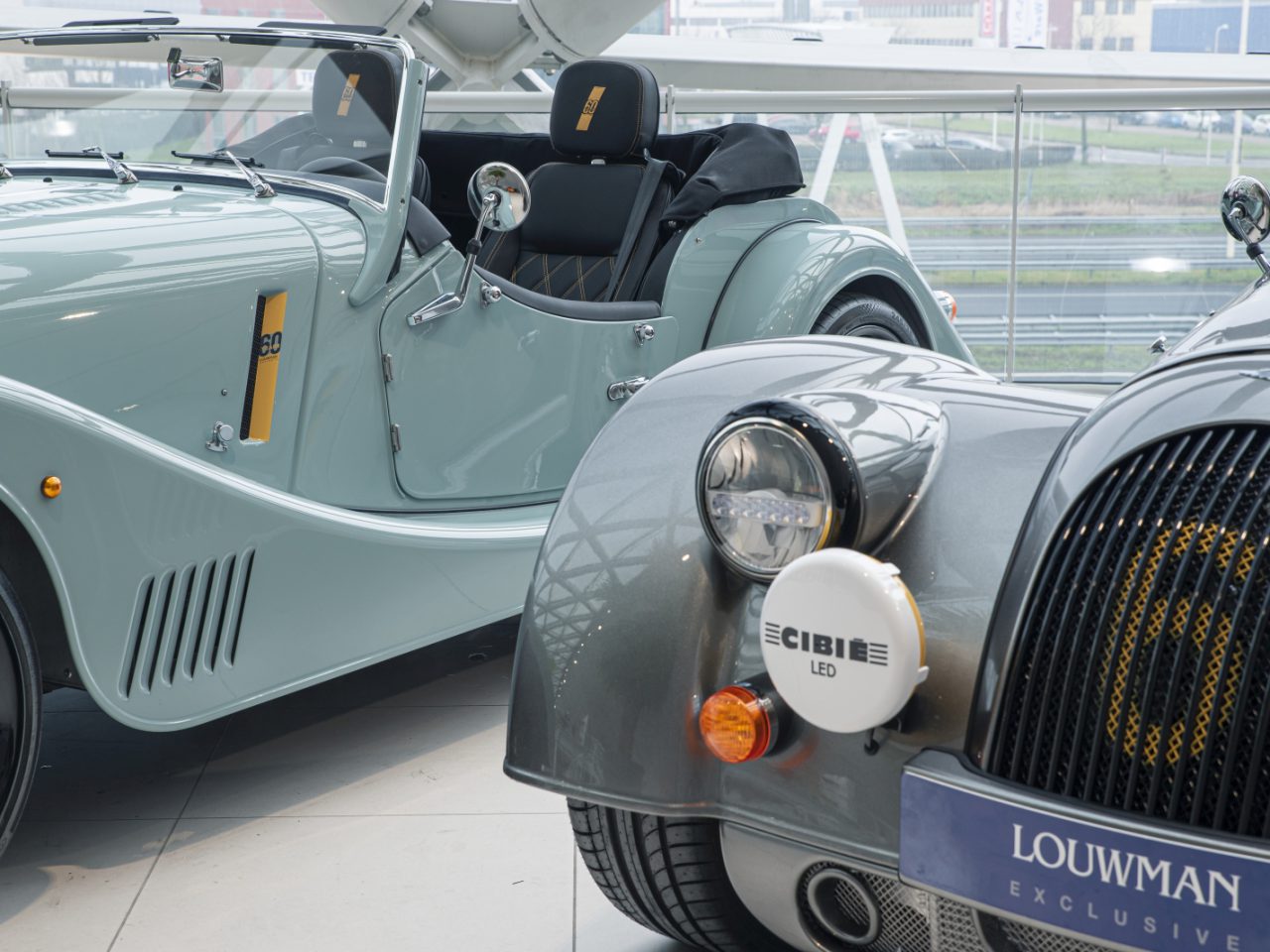 Mintgroene Morgan retro-stijl cabriolet met zwart lederen stoelen tentoongesteld in een autoshowroom.