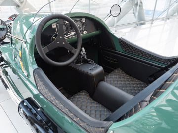 Binnenaanzicht van een groene vintage sportwagen van Morgan, met de nadruk op het stuur en de lederen stoelen.