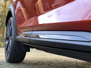 Close-up zijaanzicht van een rode Nissan Juke, gericht op het voorwiel en de zijskirt.